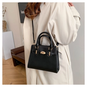 Detail of black faux leather handbag with gold buckle closure and dual handle straps