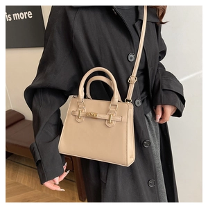 Crossbody view of beige leather satchel with dual handles and gold turn-lock buckle