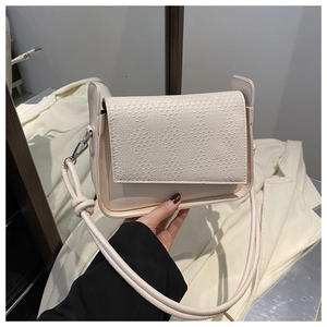Detail of cream crossbody bag featuring a woven textured flap and silver metal clasps