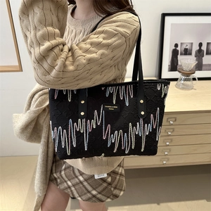 Black quilted tote bag with colorful wavy embroidery and leather logo on shoulder strap
