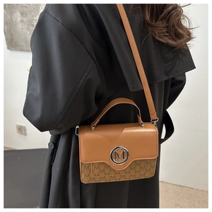 Detail of a brown leather crossbody bag with M logo pattern and silver metal buckle
