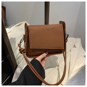 Macro view of brown textured crossbody bag with silver hardware and woven detail