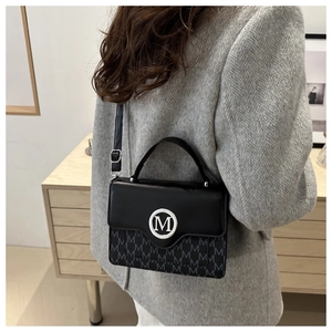 Detail of black leather handbag with silver M logo and monogram pattern on wool coat