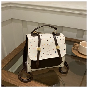 Polka dot flap backpack with gold hardware and logo detail on a glass side table