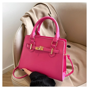 Detail of fuchsia structured handbag with gold turn-lock on beige leather seat