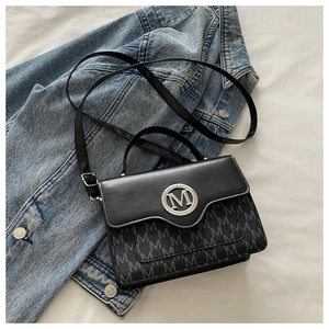 Detail of black crossbody bag with M monogram print and silver metal logo on denim jacket