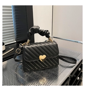 Dettaglio borsa nera trapuntata a V con fibbia a cuore dorata e manico a scrunchie