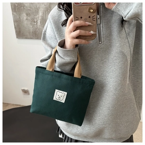 Detail of green canvas bucket bag featuring a cute bear patch and sturdy top handles
