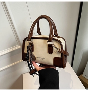 Detail of a chic cream Boston bag with brown leather handles and a woven rope charm