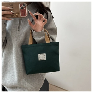 Detail of green canvas bucket bag with cute bear patch and brown woven handle strap