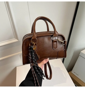 Detail of vintage brown leather Boston bag with gold lettering and woven charm