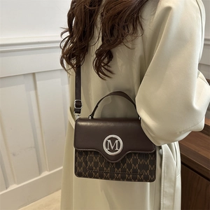 Brown leather crossbody square bag with M-pattern canvas on a model in vintage interior