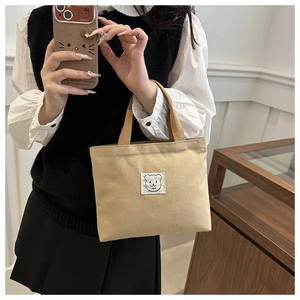 Detailed shot of beige canvas bucket bag with cartoon bear patch and soft carry handle