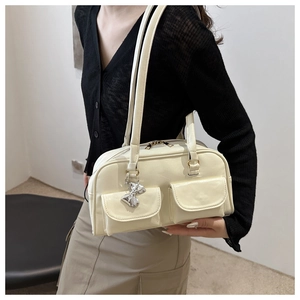 Detail der cremeweißen Lackledertasche mit silbernem Schleifenanhänger und Fronttaschen