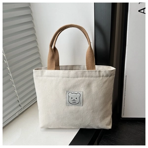 Detailed view of canvas bucket bag with brown woven handle and cute bear logo patch