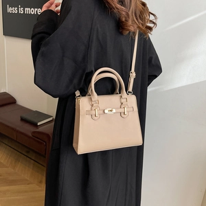 Minimalist beige leather handbag with gold twist lock and adjustable strap