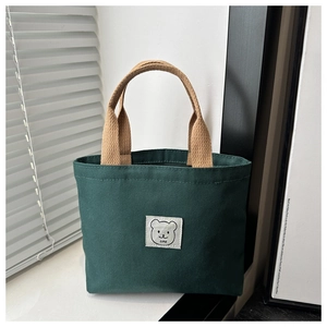 Detailed close-up of dark green canvas bucket bag featuring a cute bear label on a windowsill