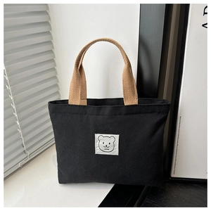 Close-up of a black canvas bucket bag with brown woven handles and a cartoon bear patch
