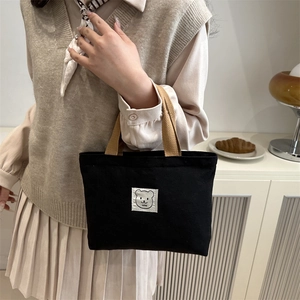Minimalist black canvas bucket bag with bear patch and khaki handles in a cozy home setting