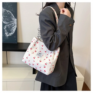 Detail of white cherry print canvas tote bag with metal chain strap on a model