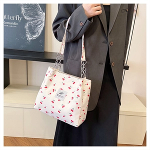 Detail of white tote bag with red cherry print, zipper closure and metal chain strap