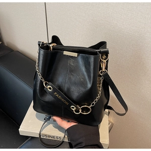 Detail view of black leather bucket bag with gold hardware and embossed fashion strap
