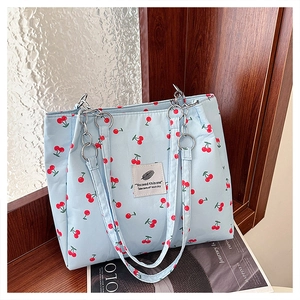 Detail of light blue tote bag with red cherry print and silver chain strap on a shelf