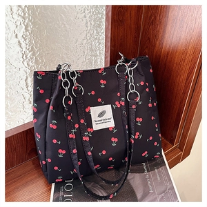 Close-up of black tote bag featuring red cherry patterns and silver chain shoulder strap