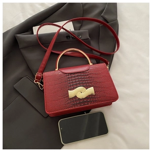 Detail of red croc-embossed small handbag with gold metal handle and magnetic buckle