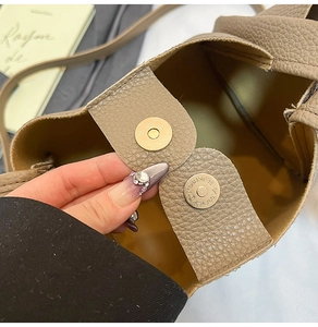Detailed close-up showing the golden magnetic snap closure on a brown leather bucket bag
