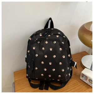 Detail of floral print backpack featuring pink flowers on black nylon fabric on a desk