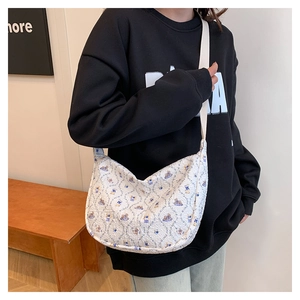 Detail of white quilted crossbody bag featuring a delicate floral pattern and broad strap