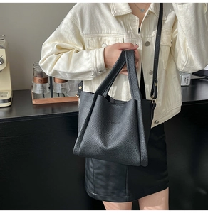 Detail of black litchi grain leather bag with embossed fashion text and gold hardware