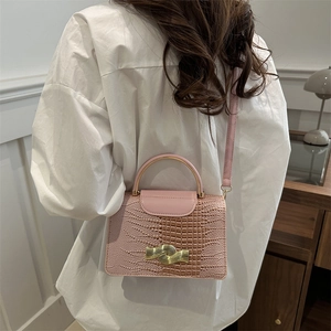 Pink crocodile-embossed handbag with gold wavy lock shown on model with white shirt