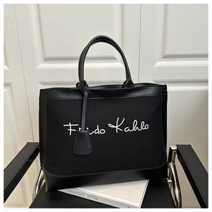 Detailed view of Frida Kahlo signature on a black canvas and leather tote bag