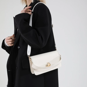 Minimalist white leather crossbody bag with gold buckle on a model in black coat