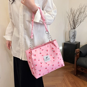 Pink tote bag with cherry print and chain strap shown in a cozy home setting