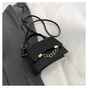 Detail of a chic black flap bag with a bold gold chain handle on a grey blazer