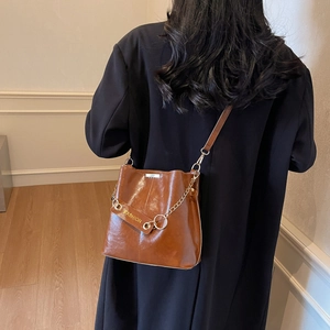 Caramel brown leather bucket bag with gold chain and crossbody strap shown on model