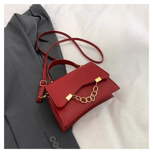 Detail of red matte leather handbag featuring bold gold chain and adjustable shoulder strap