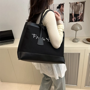 Minimalist black canvas and leather tote bag with white embroidery shown on shoulder
