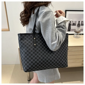 Detailed macro view of a large black tote bag with grey M-pattern and gold rivets