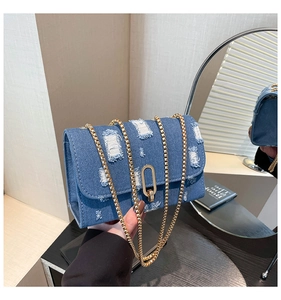 Detail of blue denim shoulder bag featuring distressed edges and gold chain strap