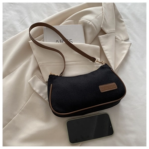 Detail of black canvas underarm bag with brown leather trim on beige suit jacket