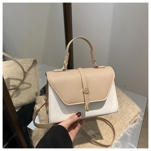 Detailed close-up of cream and white panelled handbag with golden ring buckle and top handle