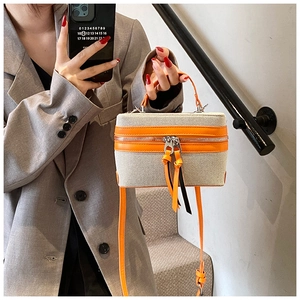 Detail of canvas box bag with orange leather trim and tassels shown with a grey blazer