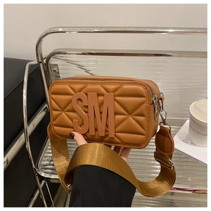 Close-up of brown quilted camera bag with bold SM logo and wide fabric shoulder strap
