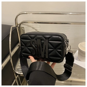 Detail of black quilted crossbody bag featuring 3D SM letters and wide nylon strap