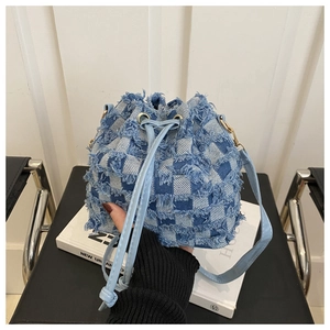 Detail of denim checkerboard bucket bag with frayed edges and drawstring closure