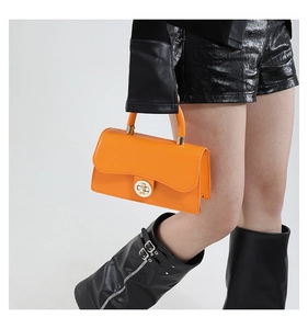 Close-up of orange crossbody bag with a round gold twist lock and smooth leather texture